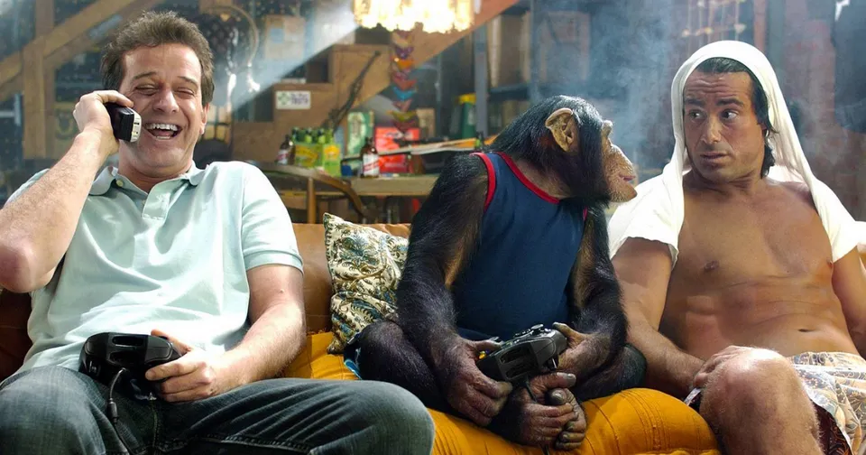 Man and two monkeys sitting on a couch, one man on the phone in a colorful living room