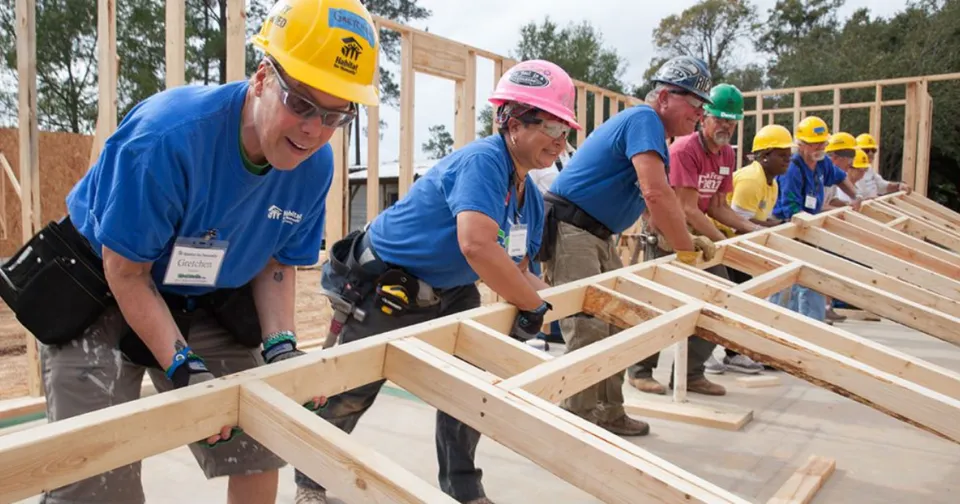 Construction workers in hard hats assembling wooden roof framing at a building site