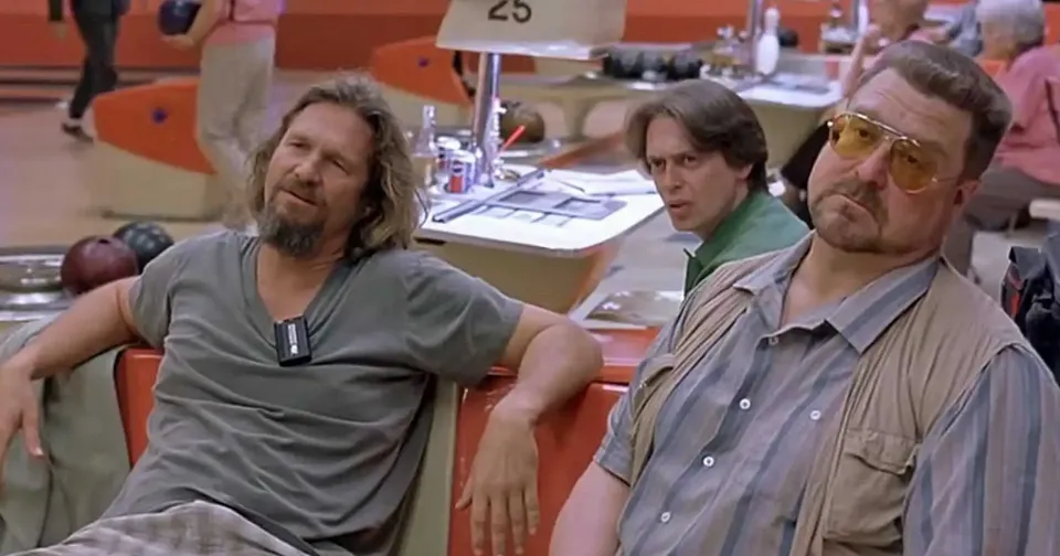 Two men sitting at tables in a cafeteria, one wearing sunglasses and both appearing relaxed.
