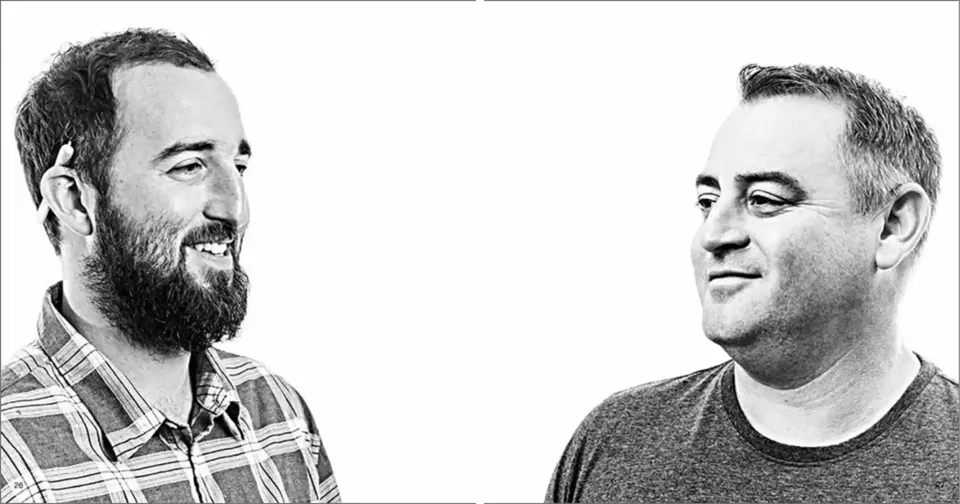 Two men facing each other and smiling in a black-and-white portrait.
