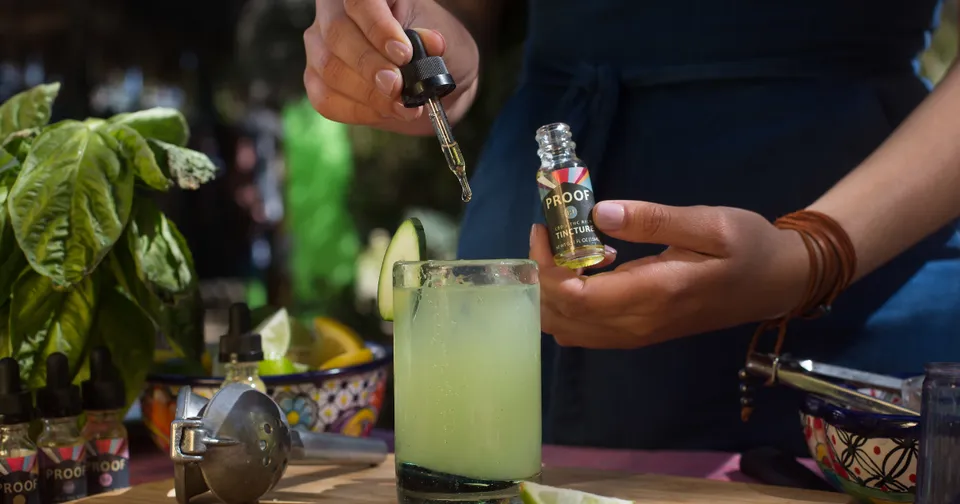 Bartender pouring a light green drink into a glass beside a bottle at a bar