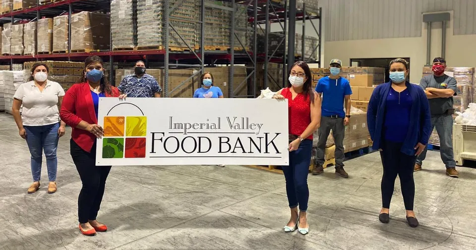 Five masked volunteers hold a Valley Food Bank banner in a warehouse-like setting.
