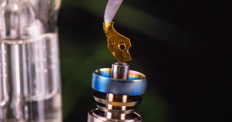 Gold atomizer coil being filled with liquid, close-up on blue and silver hardware.