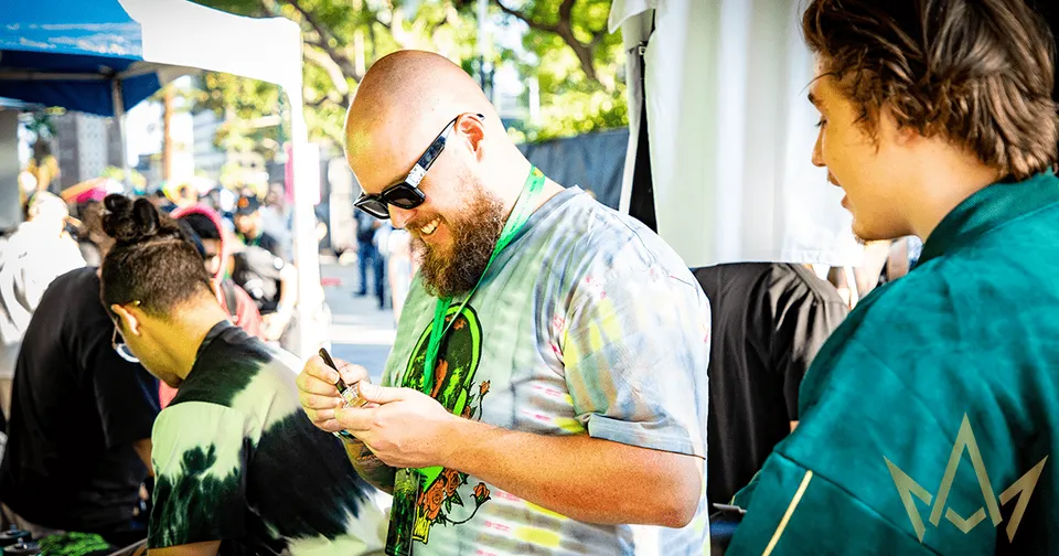 People at an outdoor event, with a man in sunglasses examining something in his hands.