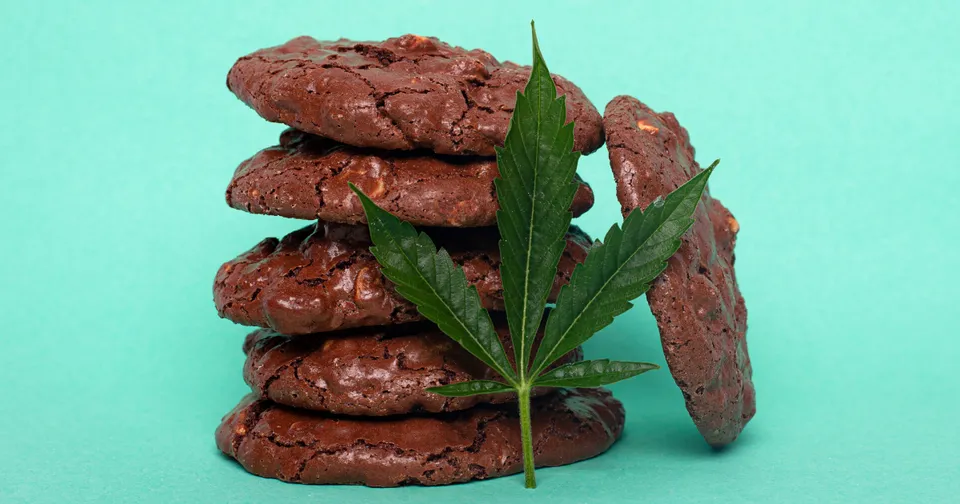 Chocolate cookies stacked with a green cannabis leaf in front on a turquoise background