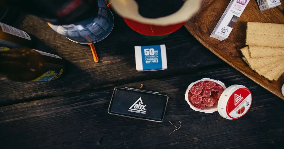 Overhead view of a dark tabletop with a card, a blue 50% item, a tin of red contents, and bread slices.