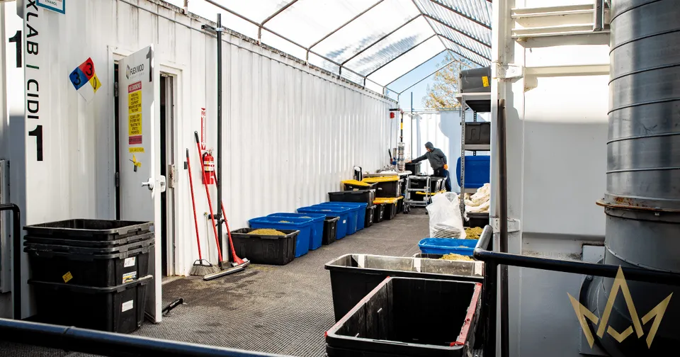 Industrial tent interior with equipment, blue bins, and red tools along a central aisle