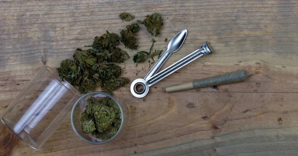 Glass pipe and metal poking tools beside loose green herb on a wooden table