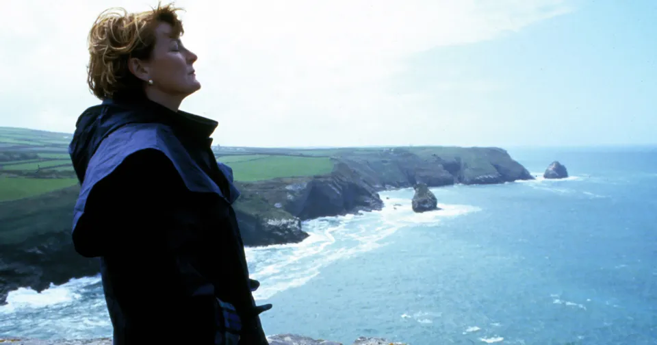 Person standing on a cliff overlooking the ocean and rocky coastline