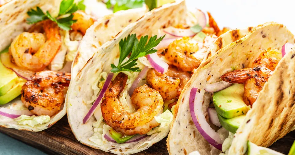 Grilled shrimp tacos with cabbage, avocado, and cilantro on a wooden board