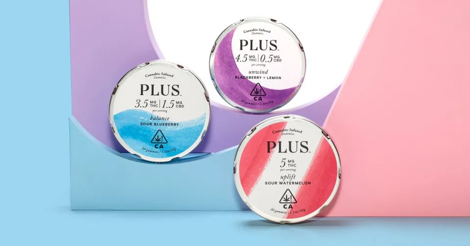 Three PLUS cosmetic jars on blue and pink background, in blue, purple, and pink labels