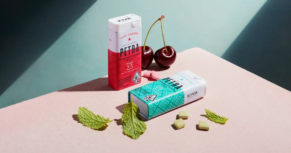 Two fruit-flavored candy packs with cherries, mint leaves, and small candy pieces on a pastel surface