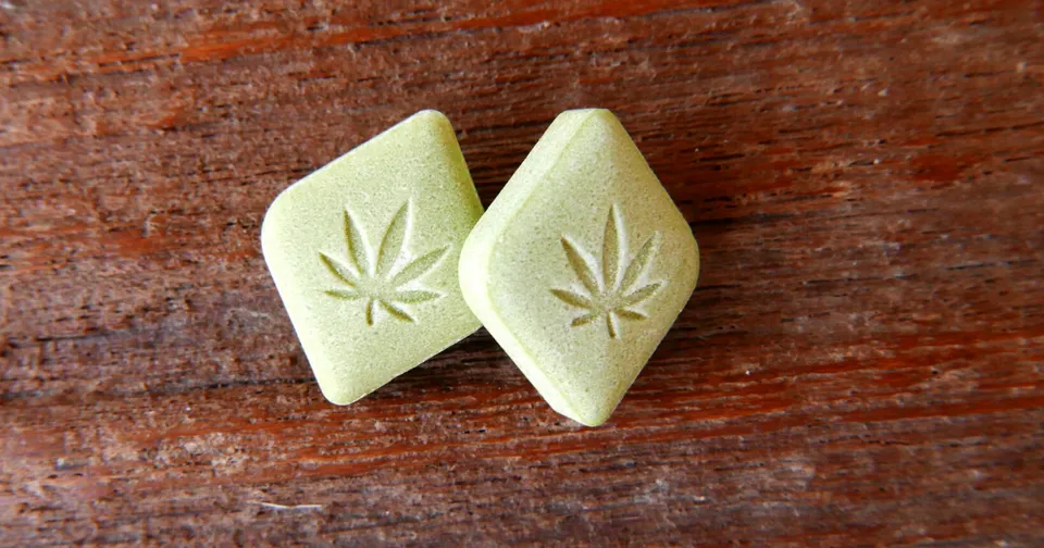 Two pale green cannabis edibles shaped like diamonds on a wooden surface