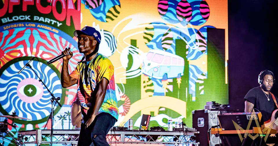 Live band performing onstage before a colorful mural backdrop at a block party event