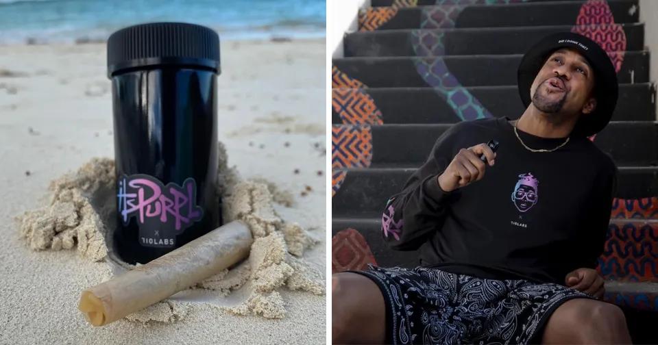 Black bottle with pink logo on sand beside a man laughing on steps, wearing a black hoodie and hat