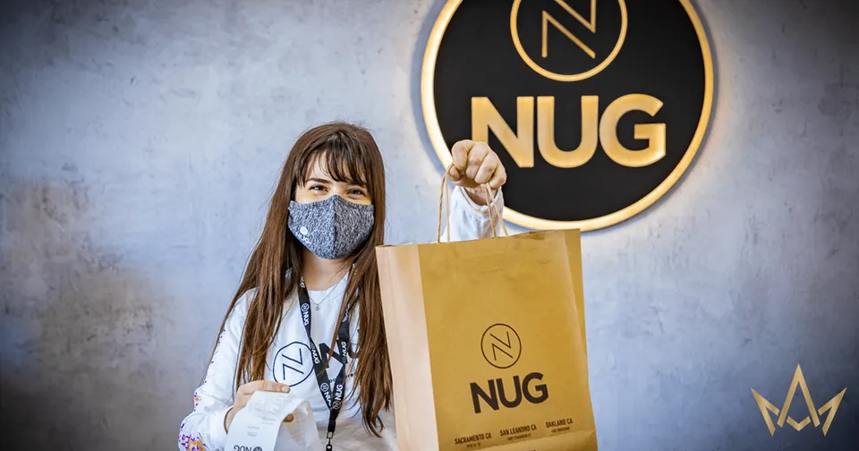 Person in a mask holds a NUG shopping bag in front of a NUG store sign.