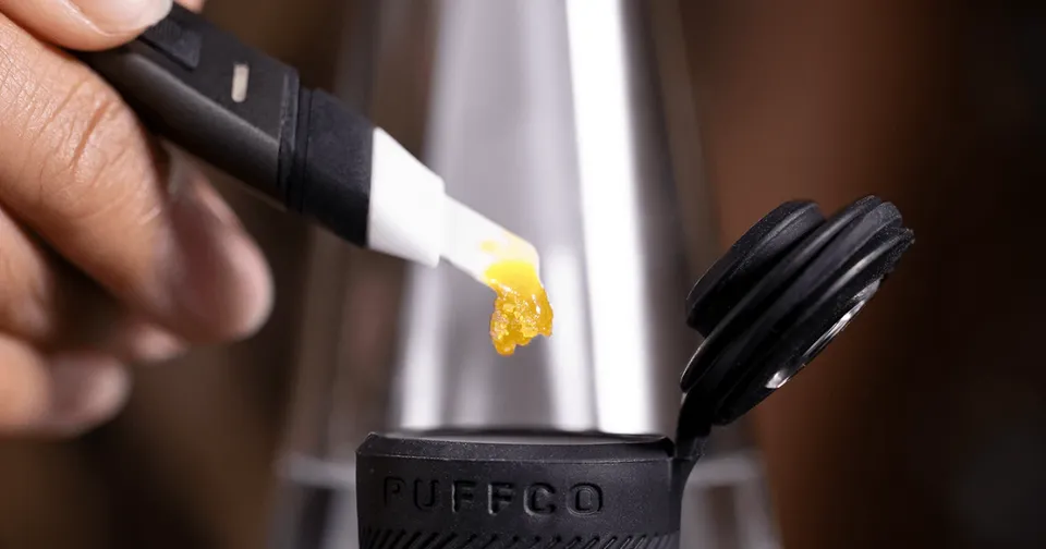 Close-up of a vape pen loading yellow cannabis concentrate into a black device cap.