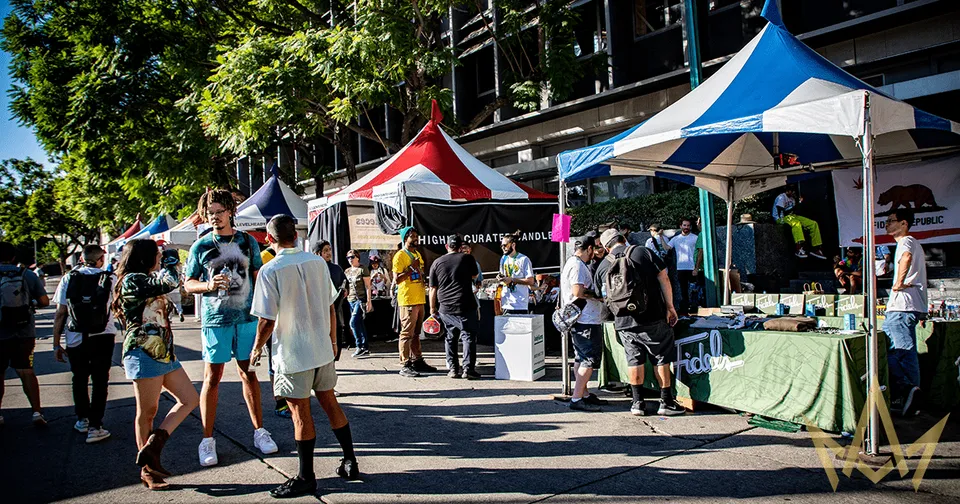 Outdoor market with people browsing vendor tents on a sunny street, including red, blue, and striped canopies.