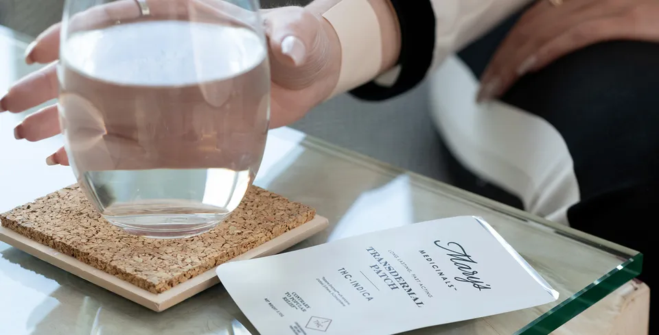 A hand holds a glass of water on a cork coaster beside a menu on a table.