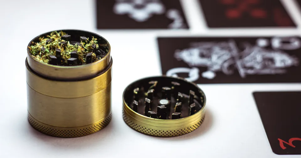 Gold metal herb grinder open beside its lid on a white surface with blurred cards in the background