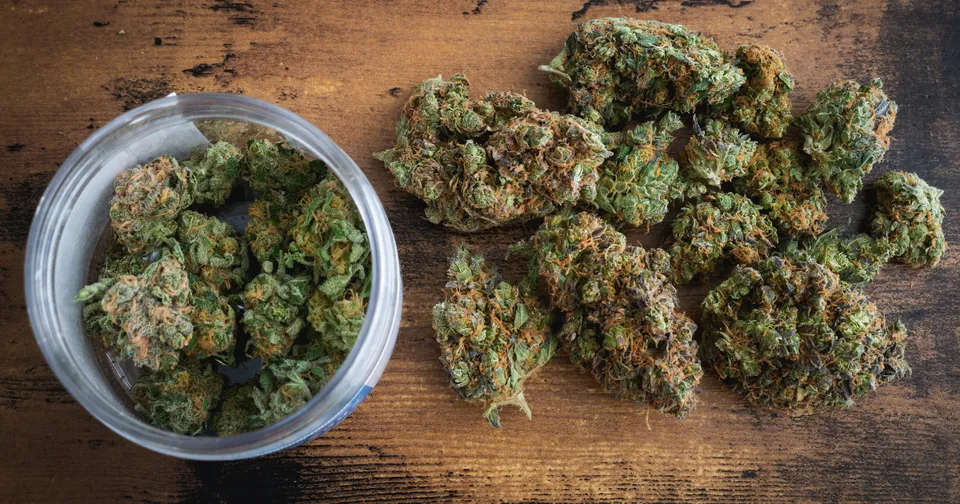 Glass jar and loose green cannabis buds on a wooden surface