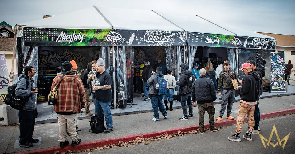 People gathered outside a graffiti-covered storefront, with tents and signs along a wet street.