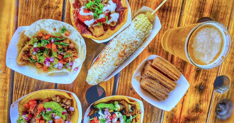Mexican street food spread with tacos, burritos, churros, and a drink on a wooden table