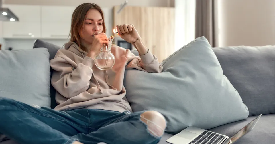 Woman sitting on a couch, sipping water beside a laptop in a cozy living room