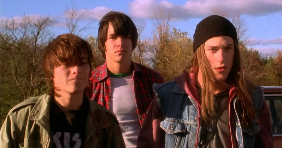Three young people outdoors in casual jackets, standing together in bright sunlight.